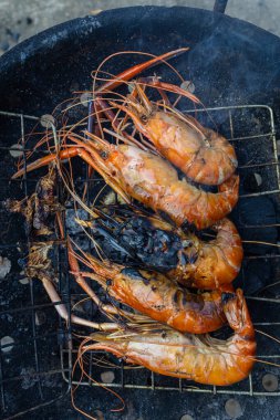 Dev nehir karidesleri ateşte kızartılıyor ve ev yapımı Asya deniz ürünleri pişiriliyor.