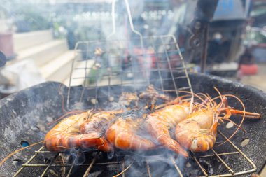 Dev nehir karidesleri ateşte kızartılıyor ve ev yapımı Asya deniz ürünleri pişiriliyor.
