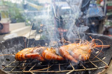 Dev nehir karidesleri ateşte kızartılıyor ve ev yapımı Asya deniz ürünleri pişiriliyor.
