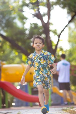 Çocuk parkında koşan küçük, mutlu bir okul çocuğu.