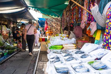Mae Klong, Tayland. 15 Haziran 2024. Turistler, Tayland 'daki Mae Klong Tren Marketi' nde taze yiyecek satan Tayland market simsarlarının trendeki şemsiyesini kapatmak için eşsiz bir turizm merkezi olan Talad Rom Hub Pazarı boyunca dolaşıyorlar..