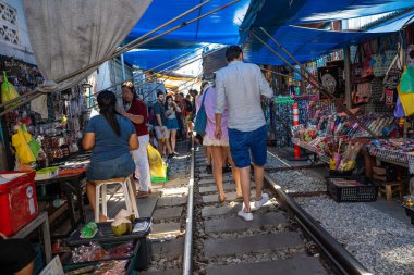 Mae Klong, Tayland. 15 Haziran 2024. Turistler, Tayland 'daki Mae Klong Tren Marketi' nde taze yiyecek satan Tayland market simsarlarının trendeki şemsiyesini kapatmak için eşsiz bir turizm merkezi olan Talad Rom Hub Pazarı boyunca dolaşıyorlar..