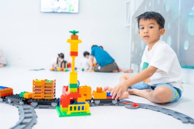 Küçük Asyalı anaokulu çocuğu beyaz oda eğitimi üzerine oyuncak tren bloğunun keyfini çıkarıyor ve öğreniyor.