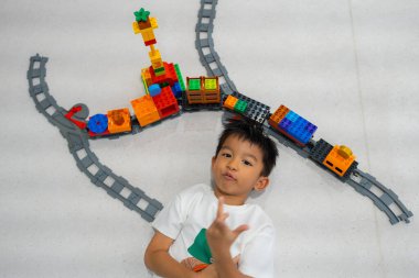 Mutlu anaokulu Asyalı çocuk beyazların eğitim odasında renkli oyuncak tren bloğu oynamaktan zevk alıyor.