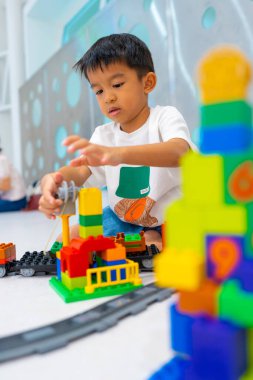Mutlu anaokulu Asyalı çocuk beyazların eğitim odasında renkli oyuncak tren bloğu oynamaktan zevk alıyor.