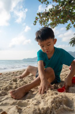 Küçük anaokulu çocuğu deniz kıyısında beyaz kumlu yaz tatilinde doğada eğleniyor.