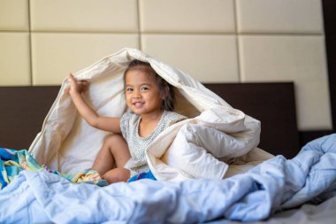 Sevimli anaokulu çocuğu uyan ve yatakta battaniyenin keyfini çıkar.