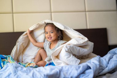 Sevimli anaokulu çocuğu uyan ve yatakta battaniyenin keyfini çıkar.