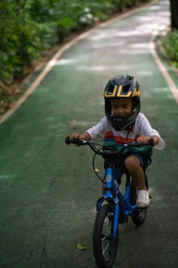 Küçük anaokulu çocuğu hafta sonu şehir parkında bisiklet sürmekten zevk alıyor.