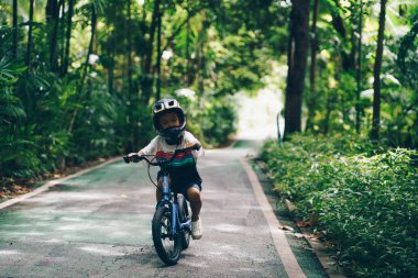 Küçük anaokulu çocuğu hafta sonu şehir parkında bisiklet sürmekten zevk alıyor.