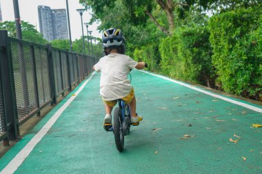 Küçük anaokulu çocuğu hafta sonu şehir parkında bisiklet sürmekten zevk alıyor.