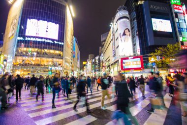 Shibuya Kavşağı 'nda gece vakti yürüyen insanların bulanık arka planı.