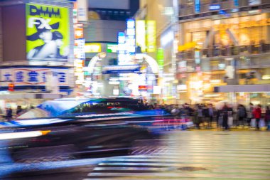 Shibuya Kavşağı 'nda gece vakti yürüyen insanların bulanık arka planı.