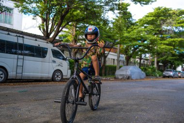 Küçük Asyalı çocuk şehir merkezindeki yol kenarında bisiklet antrenmanının keyfini çıkar.