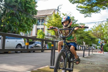 Küçük Asyalı çocuk şehir merkezindeki yol kenarında bisiklet antrenmanının keyfini çıkar.