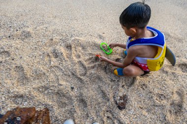 Küçük Asyalı çocuk kumsalda kum oynuyor plaj oyuncağıyla dışarıda eğleniyor.