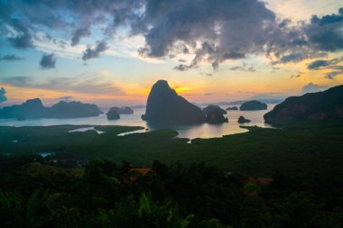 Sabah güneşinin doğuşu. Deniz koyundaki ormanın üzerinde bulutlu ve doğa manzaralı bir gökyüzü.