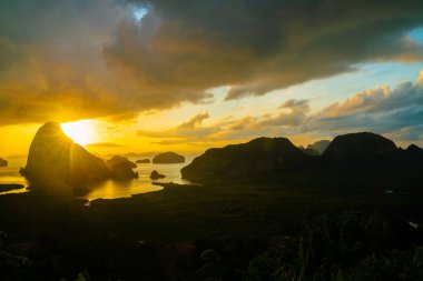 Sabah güneşinin doğuşu. Deniz koyundaki ormanın üzerinde bulutlu ve doğa manzaralı bir gökyüzü.