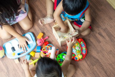 Çocuk grubu, çocuk odasının zemininde ahşap bir oyuncak tasarımcısıyla, odada oynayan çocuklarla oynuyor.