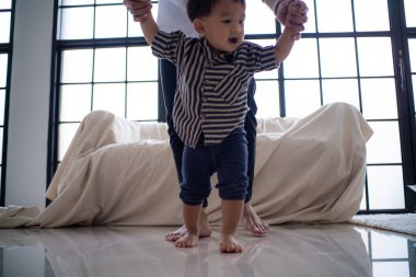 Küçük Asyalı çocuk babasıyla sıcak odada ilk adım pratiği yapıyor.