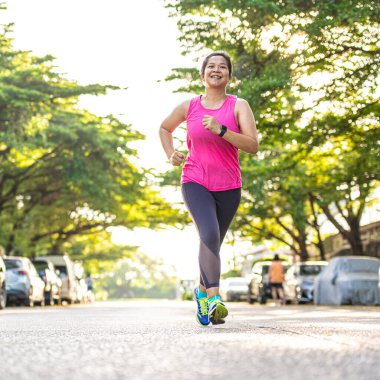 Genç ve çekici Asyalı kadının gülümseyen portresi sabahın erken saatlerinde şehir parkında koşuyor..