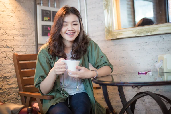 Asian smiling woman drinking coffee siting on chair in cafe