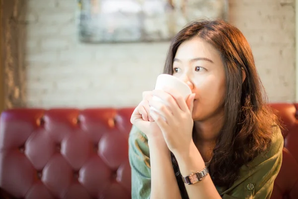 Ελκυστική νεαρή γυναίκα που κάθεται στον καναπέ πίνοντας καφέ — Φωτογραφία Αρχείου