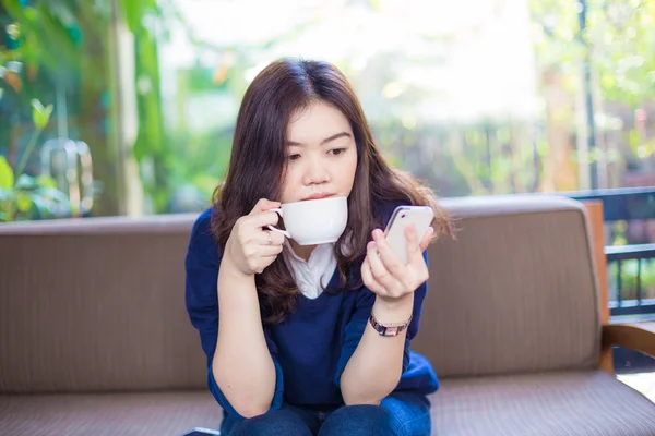 Женщина пьет кофе и пользуется мобильным телефоном — стоковое фото