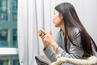 Yatak arka perde ve pencere ile akıllı telefon kullanan genç kadın