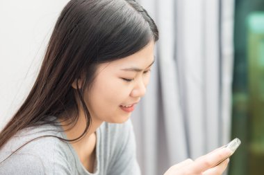 Rahat Asyalı kadın evde modern yatak odasında cep telefonu kullanarak