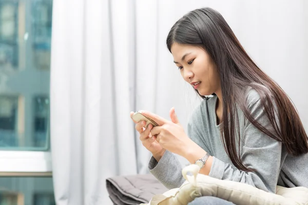 Young woman using smart phone on the bed background with curtain and window