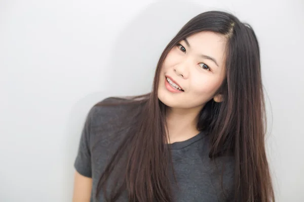 Bautiful asiatische Mädchen lächelnd auf grauem Hintergrund Studio — Stockfoto