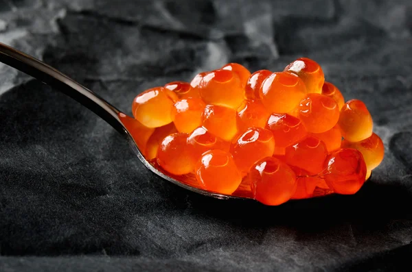 Red caviar in a metal spoon on a black background Stock Photo