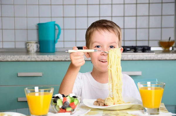 Glad pojke sitter vid matbordet och letar spaghetti — Stockfoto