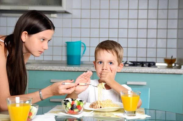 Sister trying to feed her brother. he resists and repels fork wi — Stock Photo, Image