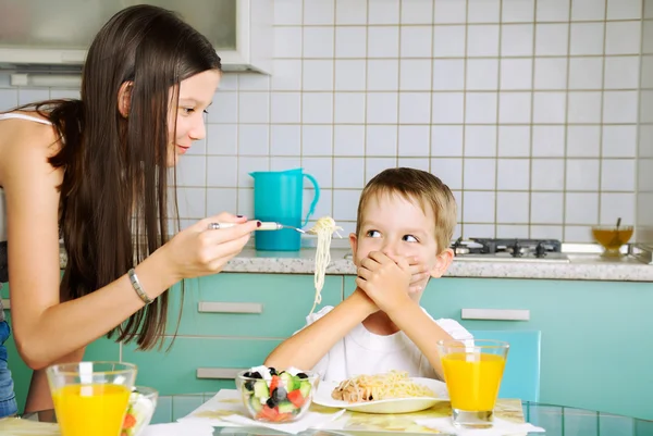 Smiling girl trying to feed little boy. he closed mouth by the h — Stock Photo, Image