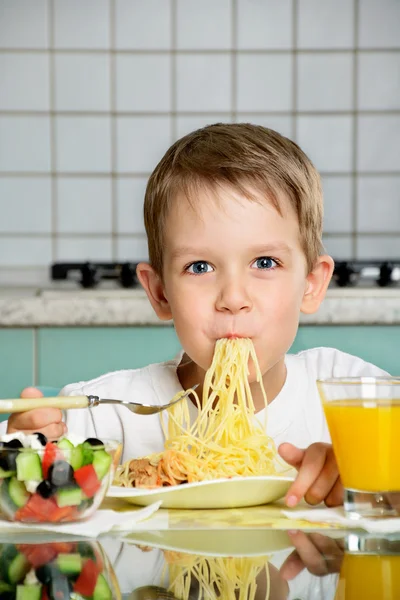 Uśmiechnięty chłopiec jedzenie spaghetti i trzyma widelec — Zdjęcie stockowe