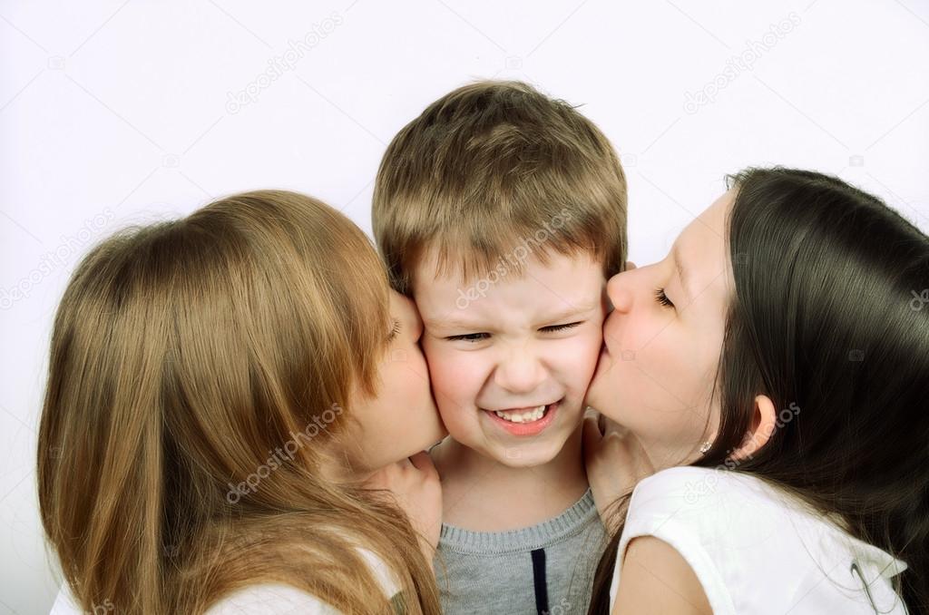 two girls kissing little angry boy on the light background