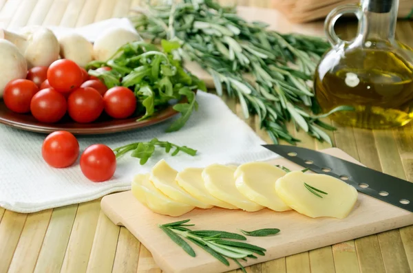 Sliced cheese, tomatoes and herbs on a kitchen table — Stock Photo, Image