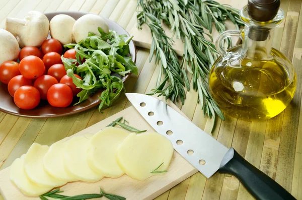 Sliced cheese, tomatoes, mushrooms and herbs on a kitchen table — Stock Photo, Image