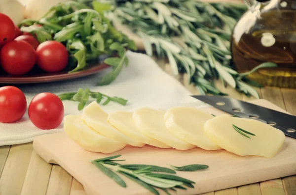 Tinted image sliced cheese, tomatoes and herbs on a kitchen tabl — Stock Photo, Image