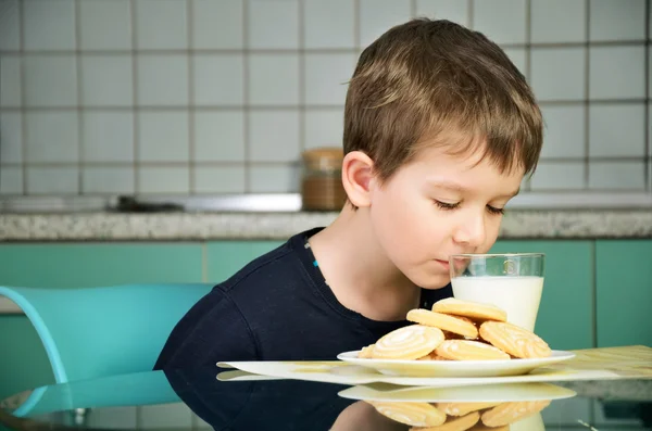 Cheerful little boy sniffs with pleasure milk, sitting at the di — Stock Photo, Image