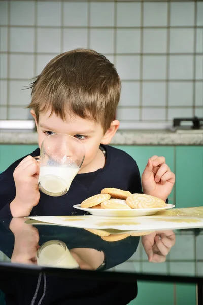 Menino alegre bebendo leite, sentado na mesa de jantar . — Fotografia de Stock