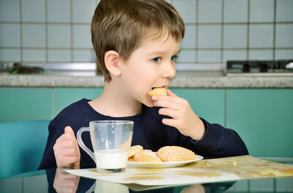 Μικρό αγόρι δαγκώνει τα cookies, κάθεται στο τραπέζι του δείπνου. Horizont — Φωτογραφία Αρχείου