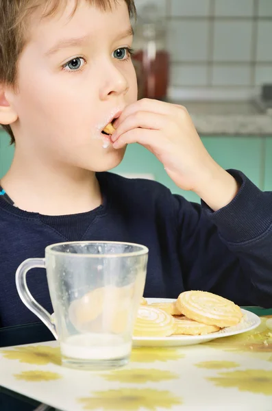 Little boy eating cookies, sitting at the dinner table. vertical — Stock Photo, Image