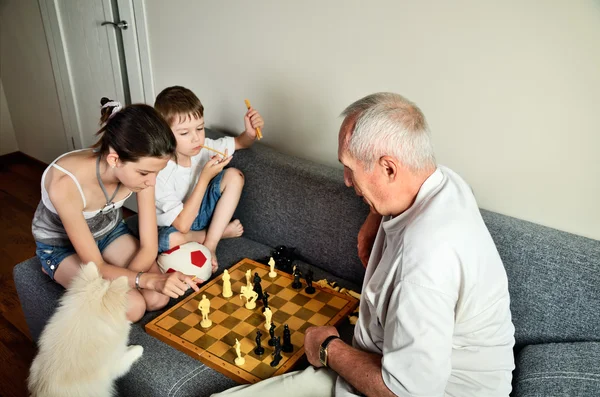 Grandchildren with grandpa playing chess — Stock Photo, Image