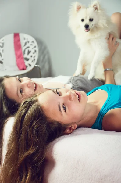 Imagem matizada duas meninas com um Pomeranian leigos na cama e laug — Fotografia de Stock