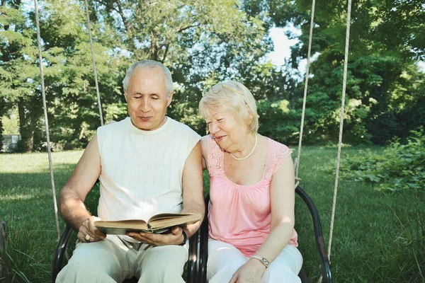 Smiling mature man and  woman 65-69 years old reading a book in — Stock Photo, Image