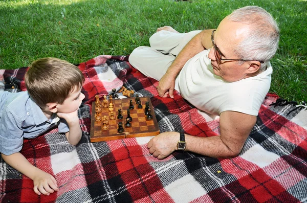 Niño y su abuelo juegan al ajedrez en el parque —  Fotos de Stock