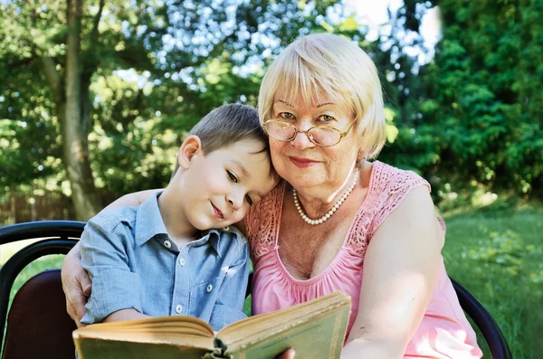 Niño sonriente y su abuela leyendo un libro en el parque —  Fotos de Stock